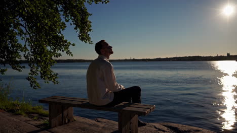 man sitting on a bench by the lake at sunset