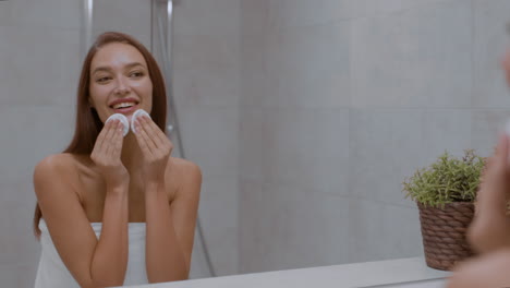 woman removing makeup with cotton pads in bathroom