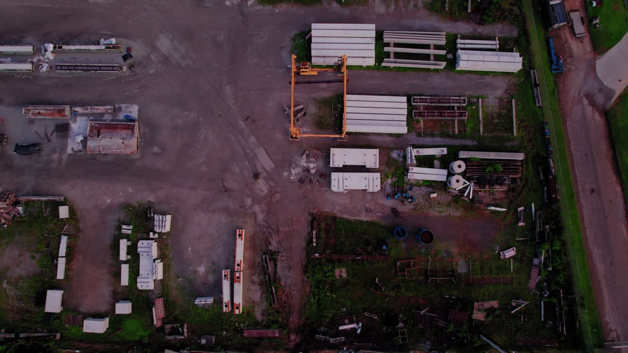Top-down drone aerial of an industrial storage yard with stacked construction materials, heavy equipment, and outdoor machinery. Alabama