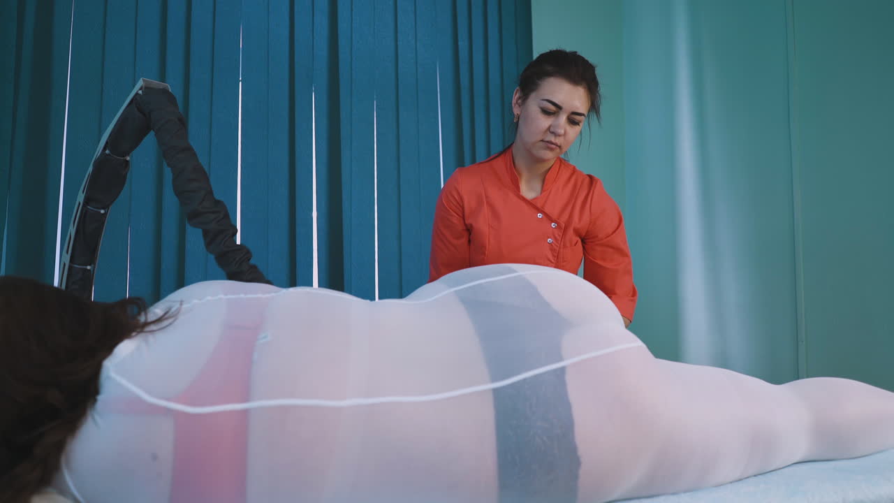 Turuncu giysili kadın genç bir hanıma vakumlu rulo masajı yapıyor.