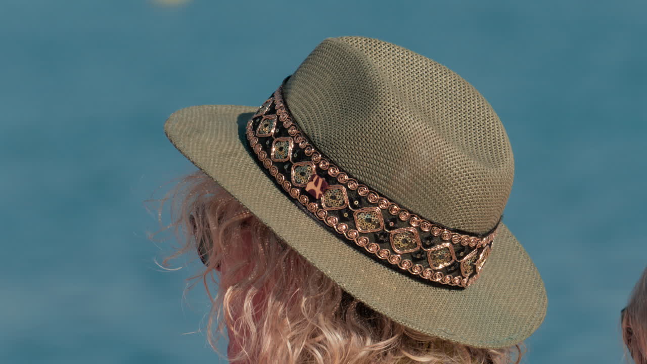 Close up of a decorated sun hat worn by a person facing the calm blue water