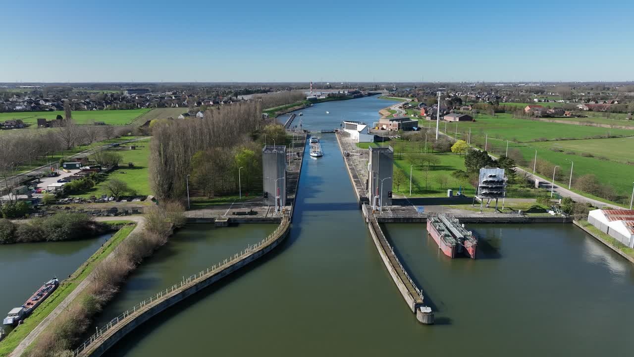 Zoom in aerial shot of Antwerp canal lock with water gates and boats, surrounded by countryside fields and industrial warehouses