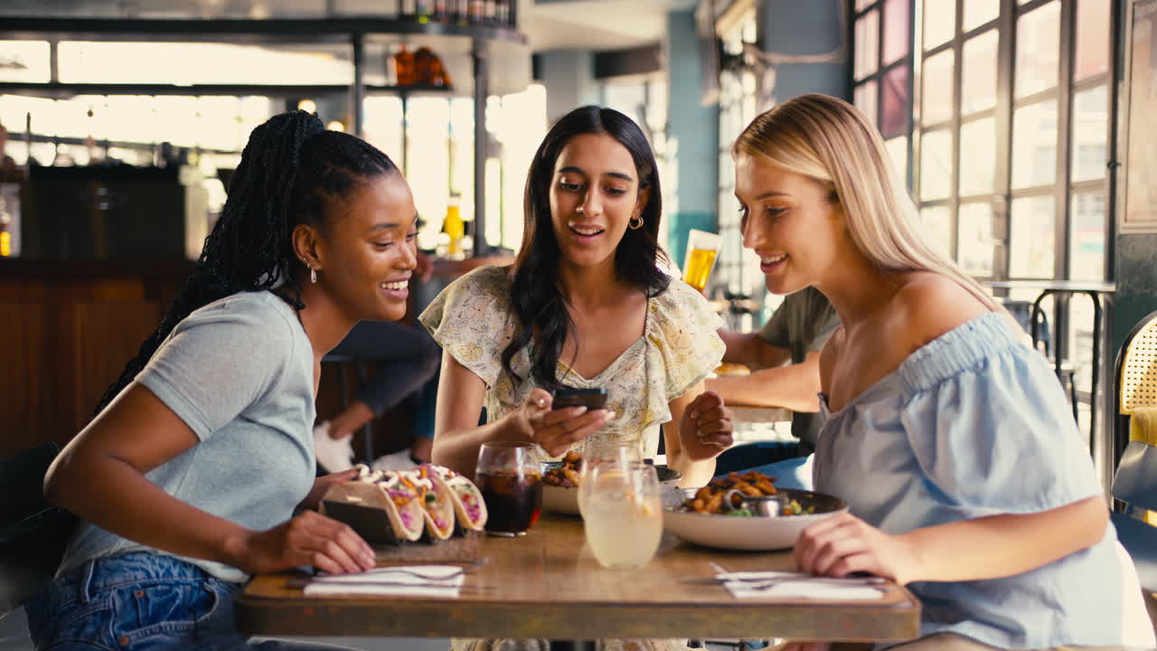 Group Of Female Friends Meeting Up In Restaurant Taking Photo Of Food On Mobile Phone