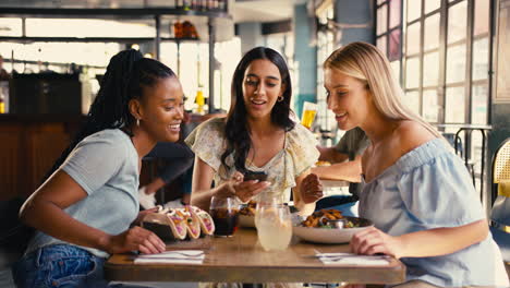 Grupo-De-Amigas-Reunidas-En-Un-Restaurante-Tomando-Fotografías-De-Comida-En-Un-Teléfono-Móvil