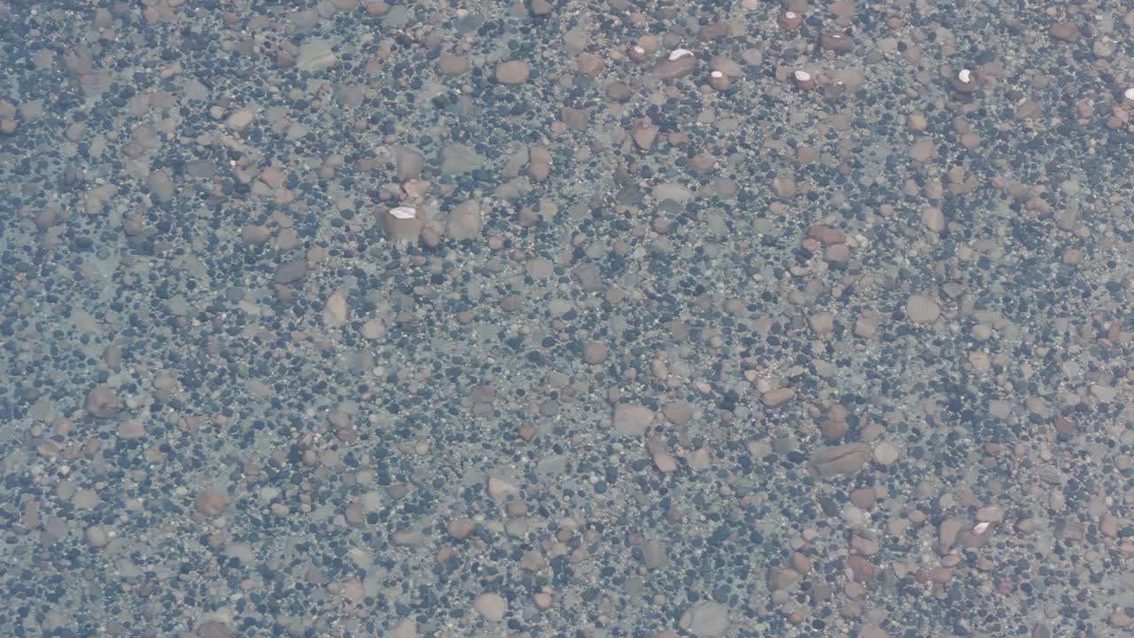 Top-down aerial view of the crystal-clear water of the Umngot River in Shnongpdeng, Meghalaya, revealing the pebble riverbed