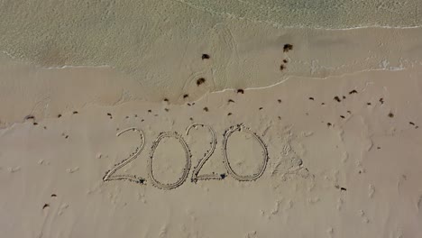 aerial camera descending on twenty twenty inscribed in the sand on a beach