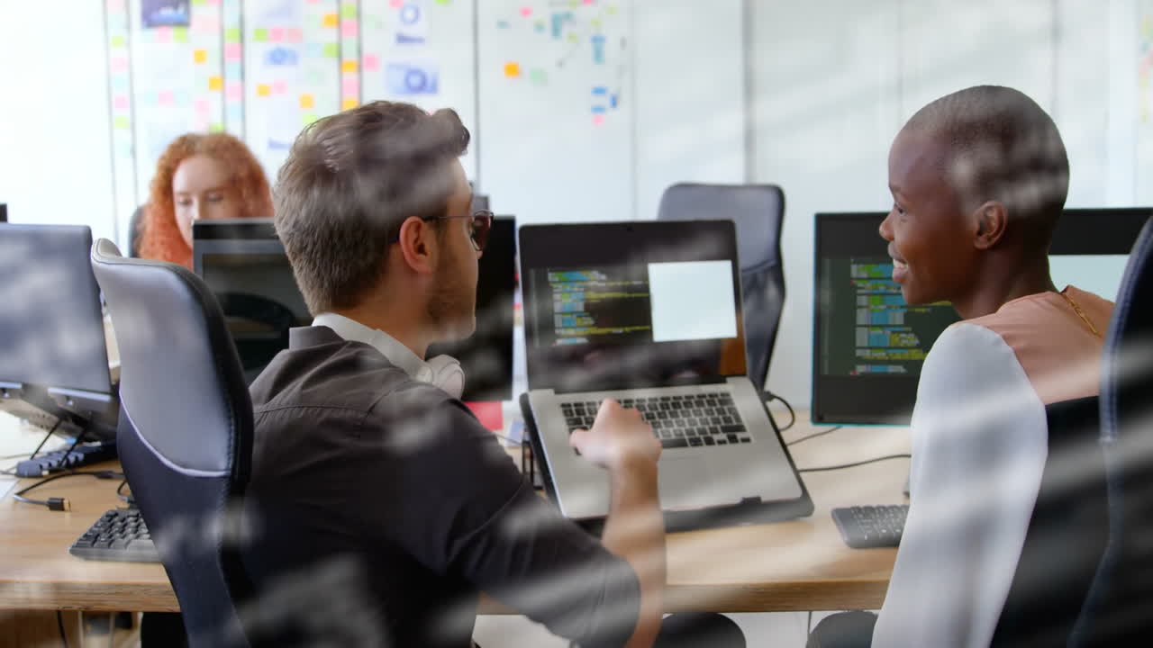 In office, colleagues discussing code on laptops with digital animation overlay