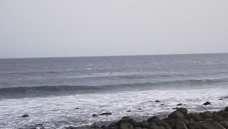 Vista-En-Cámara-Lenta-De-Un-Surfista-Solitario-Esperando-Una-Ola-En-El-Océano-Atlántico-A-Lo-Largo-De-La-Costa-De-África-Occidental