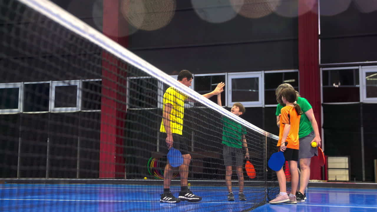 Two adults and two children high-fiving after playing pickleball on a blue, inside court