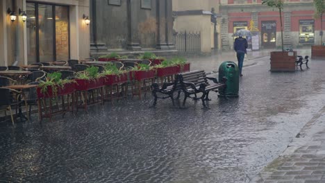 a man with an umbrella in his hand is passing the summer terrace of a restaurant in the street in rainy weather.