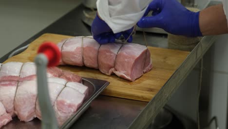 vista de la persona que prepara el lomo de carne de cerdo crudo con guantes azules en la cocina atando la carne con una cuerda