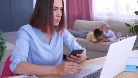 mujer trabajando en una computadora portátil en casa mientras los niños juegan en el sofá