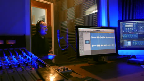 un hombre está grabando una voz en una cabina vocal de un estudio de grabación hablando por un micrófono