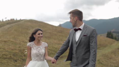 Lovely-young-newlyweds-bride-groom-walking-on-mountain-slope,-holding-hands,-wedding-couple-family