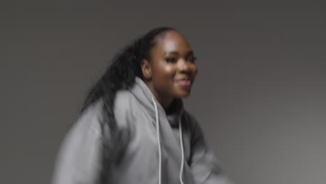 Studio-Portrait-Shot-Of-Young-Woman-Wearing-Hoodie-Dancing-With-Low-Key-Lighting-Against-Grey-Background-6