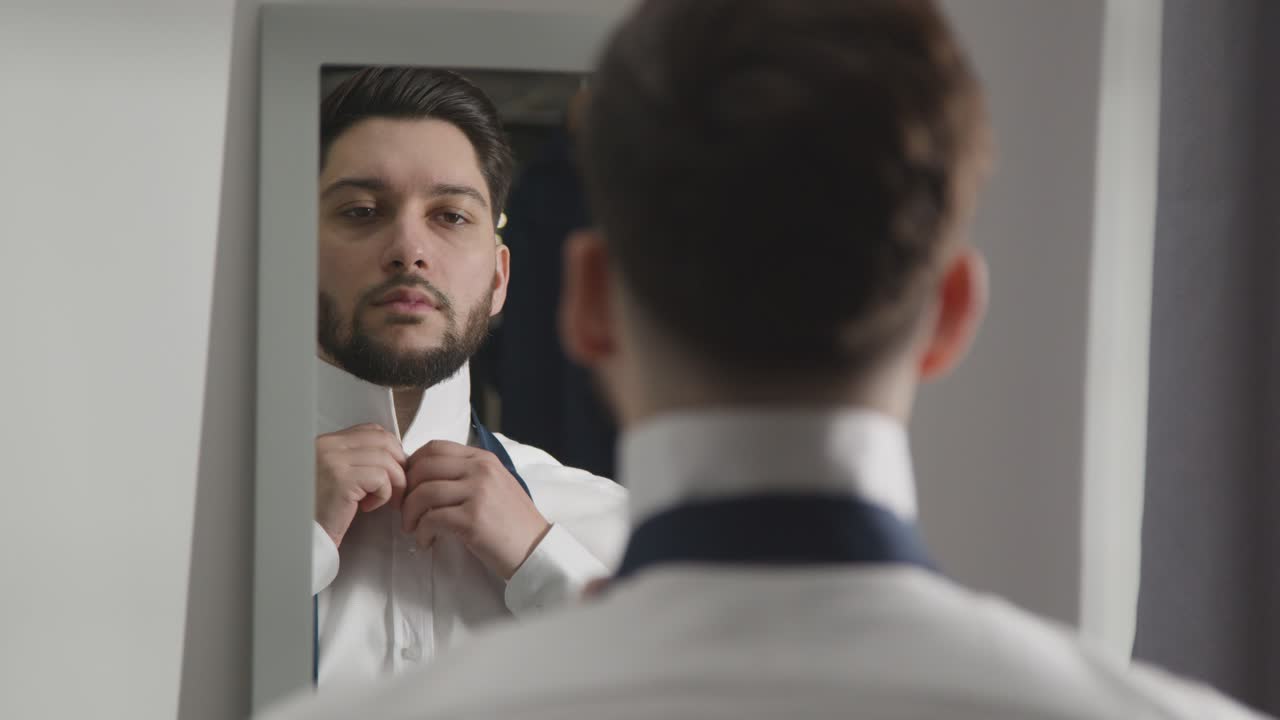 Young Man At Home Putting On Tie Ready For Job Interview Reflected In Mirror