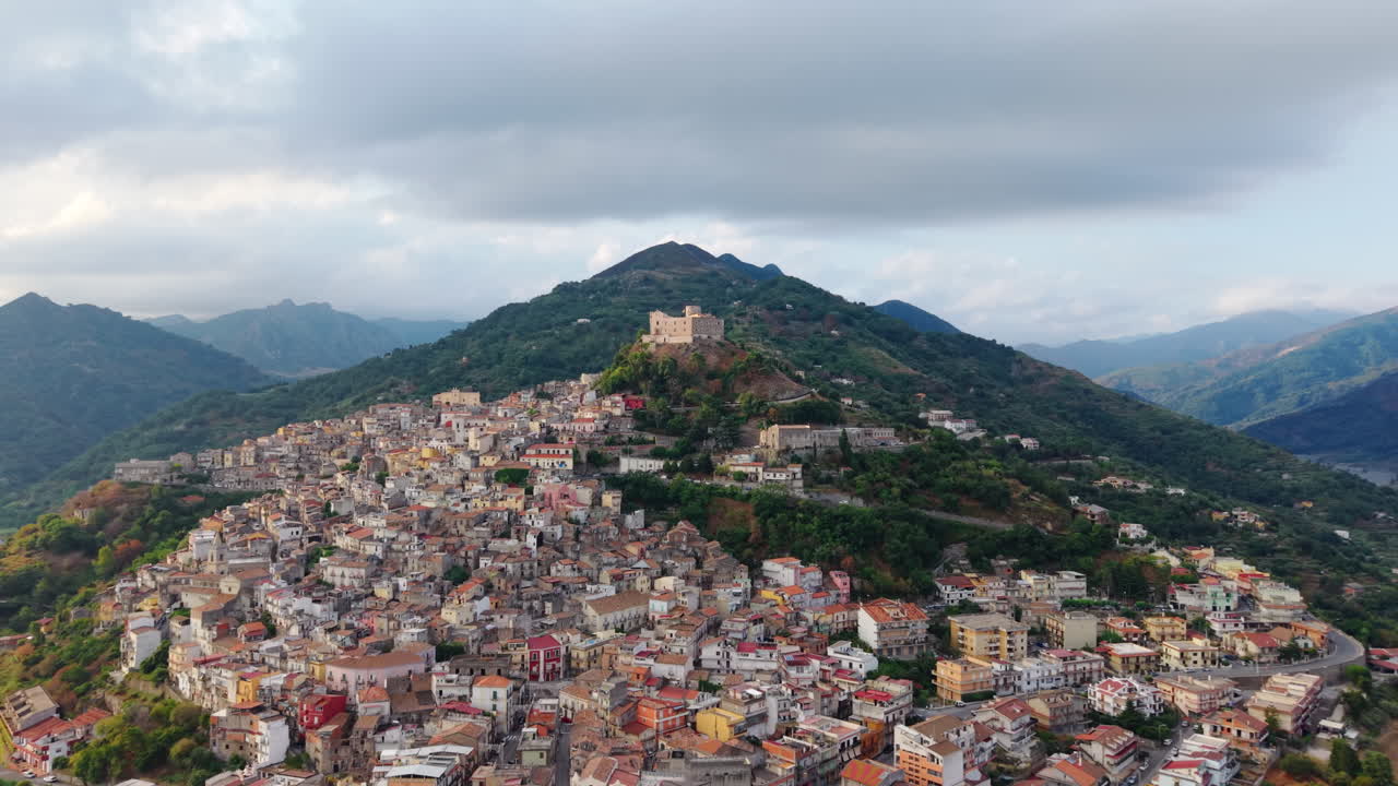Villaggio collinare della Sicilia, Italia, con edifici colorati su un versante di montagna, drone che avanza verso una cittadina rurale e la tranquilla campagna