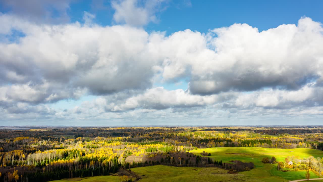 Aerial drone hyperlapse over a large area of forest with fast moving clouds in the sky. Vast views of fall colors in trees. Autumn season in countryside.