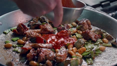 chef pours tomato on spanish paella with meat and vegetables