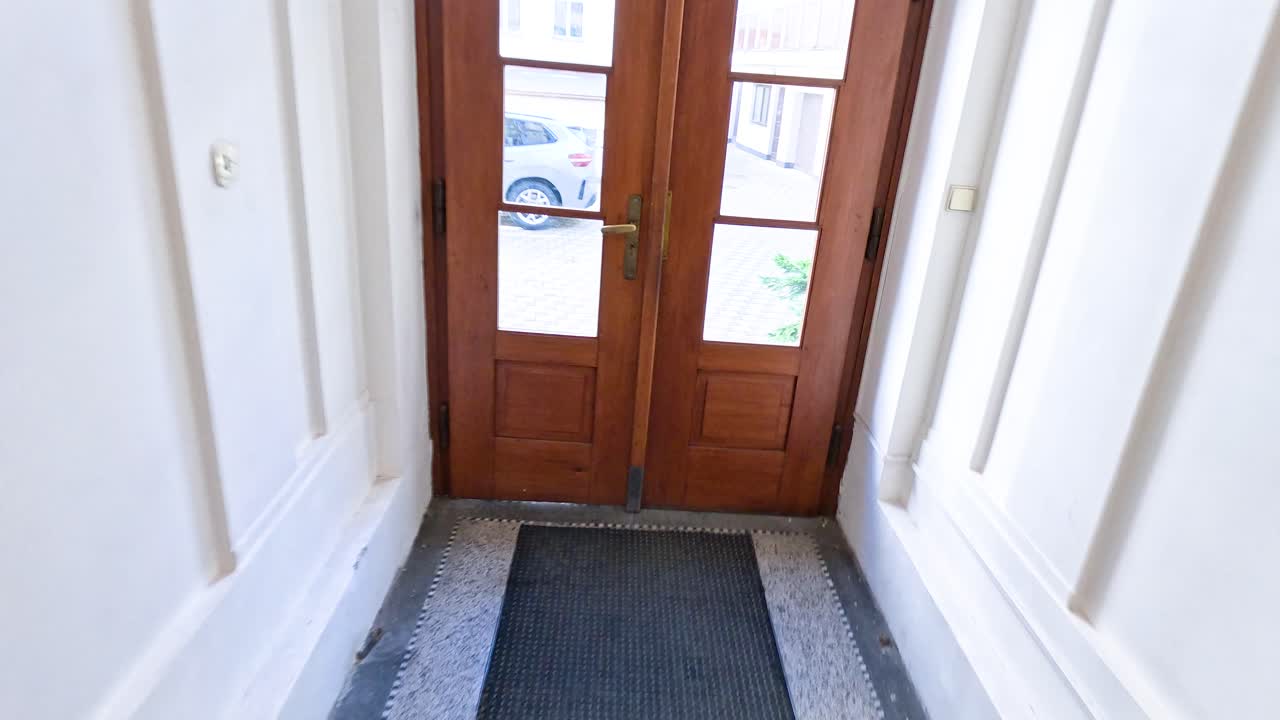 Person descends minimalist indoor staircase, exits through wooden door, natural evening light, handheld camera
