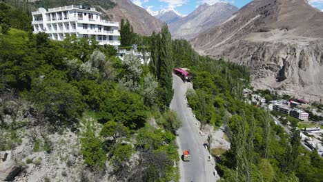 Vista-Aérea-Del-Vehículo-Rickshaw-En-La-Carretera-De-La-Ladera-En-El-Valle-De-Hunza,-Paisaje-Y-Edificios,-Disparo-De-Drones