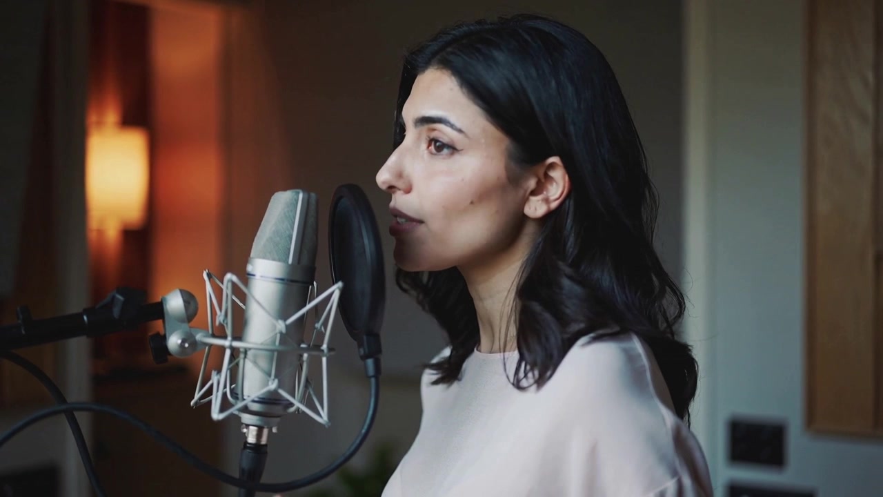 Cantante donna che registra in un microfono a condensatore con filtro anti-pop nel suo studio casalingo, indossando una camicetta.