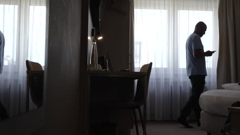 static shot of caucasian middle-aged man pacing across dark room with phone