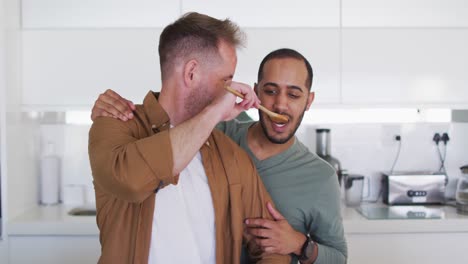 Multi-ethnic-male-same-sex-couple-preparing-food-and-tasting-in-kitchen