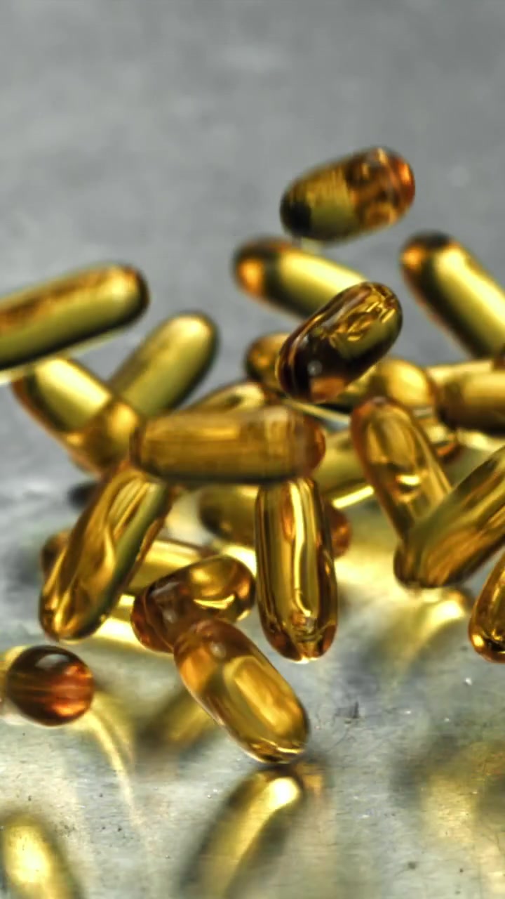 Capsule Omega-3 dorate che cadono e rimbalzano su una superficie riflettente grigia