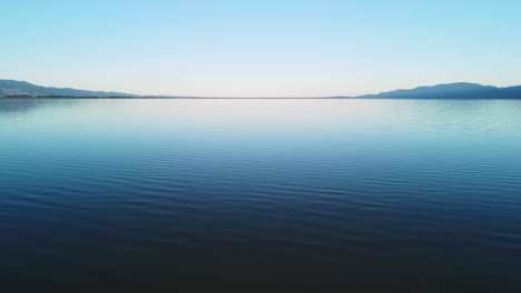 flying low over a flat lake at sunset with hills on either side