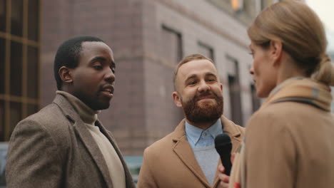 vista trasera de una periodista caucásica entrevistando a dos hombres caucásicos y afroamericanos en la calle en otoño