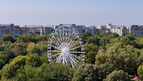 rotating drone view of a ferris wheel in oraselul copiilor park with apartment buildings in the background, bucharest, romania