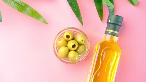 aceitunas y aceite de oliva sobre un fondo rosado