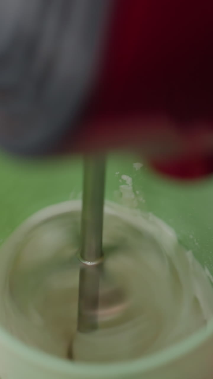 cerrar el mezclador de mano eléctrico dentro de la taza verde, mezclar ingredientes, preparar bebidas en el entorno de la cocina, encimera, fondo borroso, mezcla de líquido, elaboración de bebidas, proceso de agitación