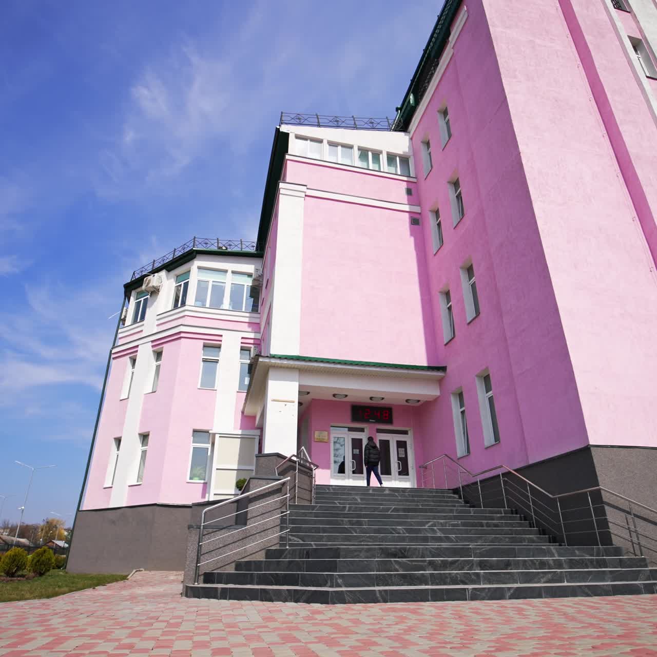 Nice pink building with grey stairs entrance. People coming up to the doors. Low angle view. Blue sky backdrop