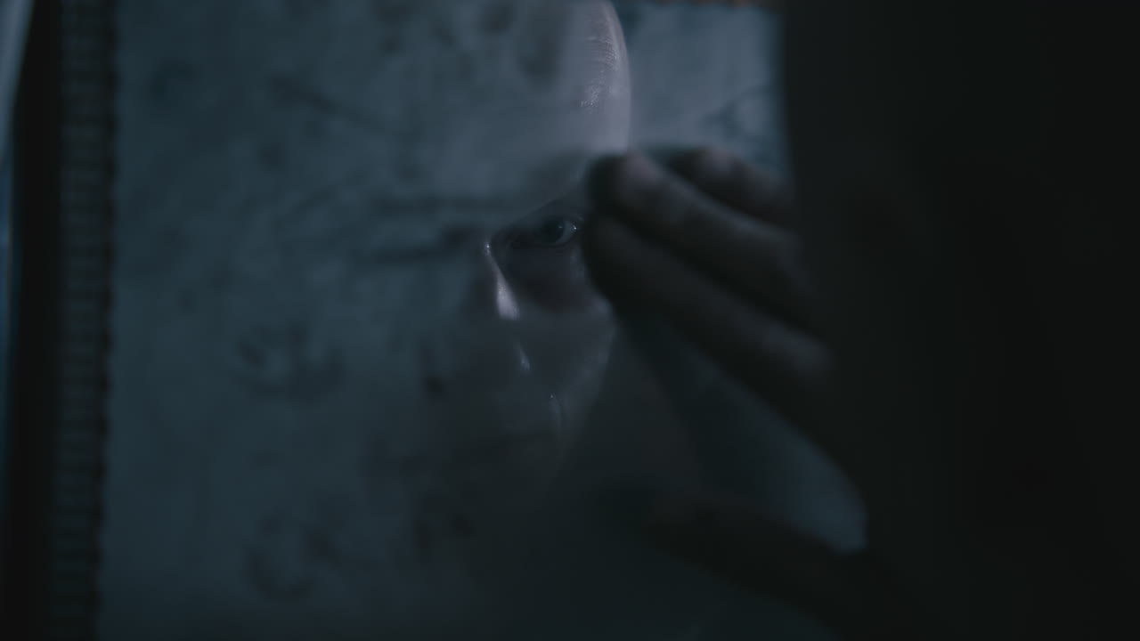 Pale bald skinny man looks into the mirror in the creepy old bathroom at night