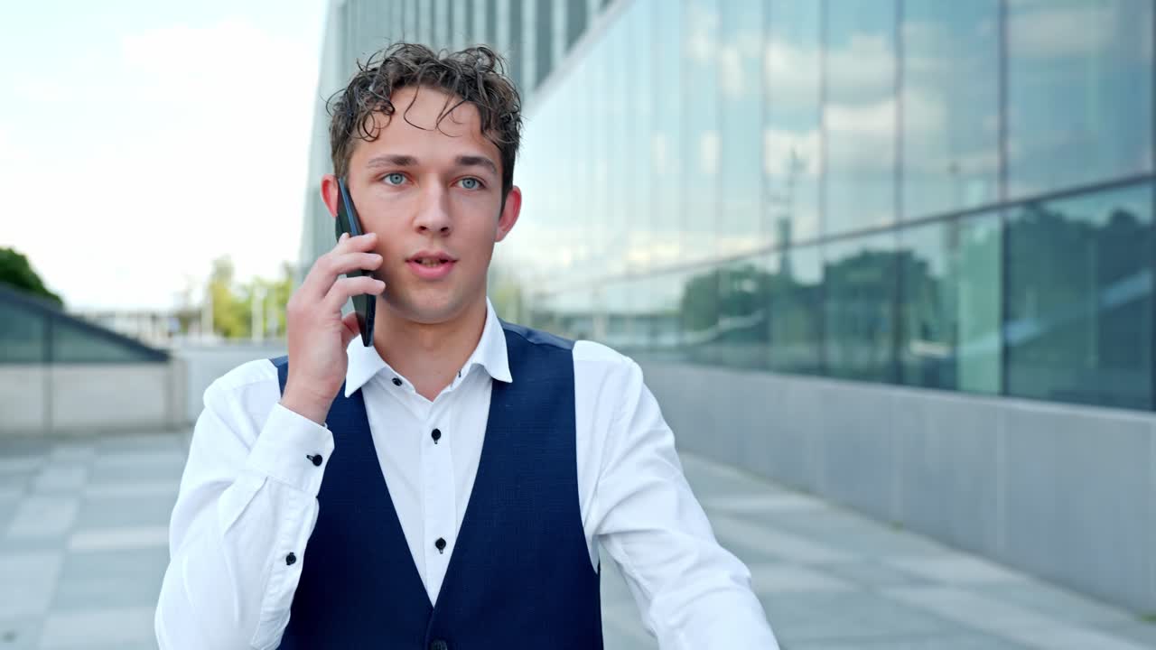 Young businessman having phone call, walking on city street, communicating with client, discussing business, connecting using wireless technology, follow slow motion shot