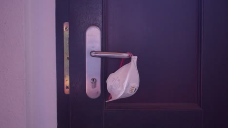 young adult man taking hanging respirator mask from the door handle and opens the door to going outside.