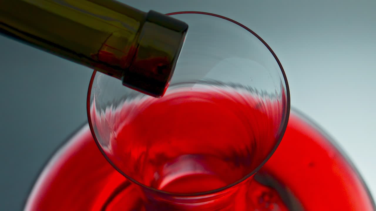 Primo piano di gocce di vino che cadono su una caraffa di vetro. Una goccia che schizza dal collo della bottiglia.