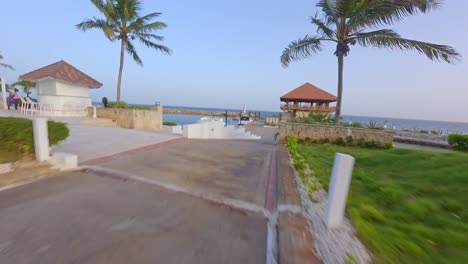 Aerial-fpv-flight-along-promenade,-marina-with-parking-yachts-and-Restaurant-Captain-Kidd-in-La-Romana-at-sunset---orbiting-drone-shot