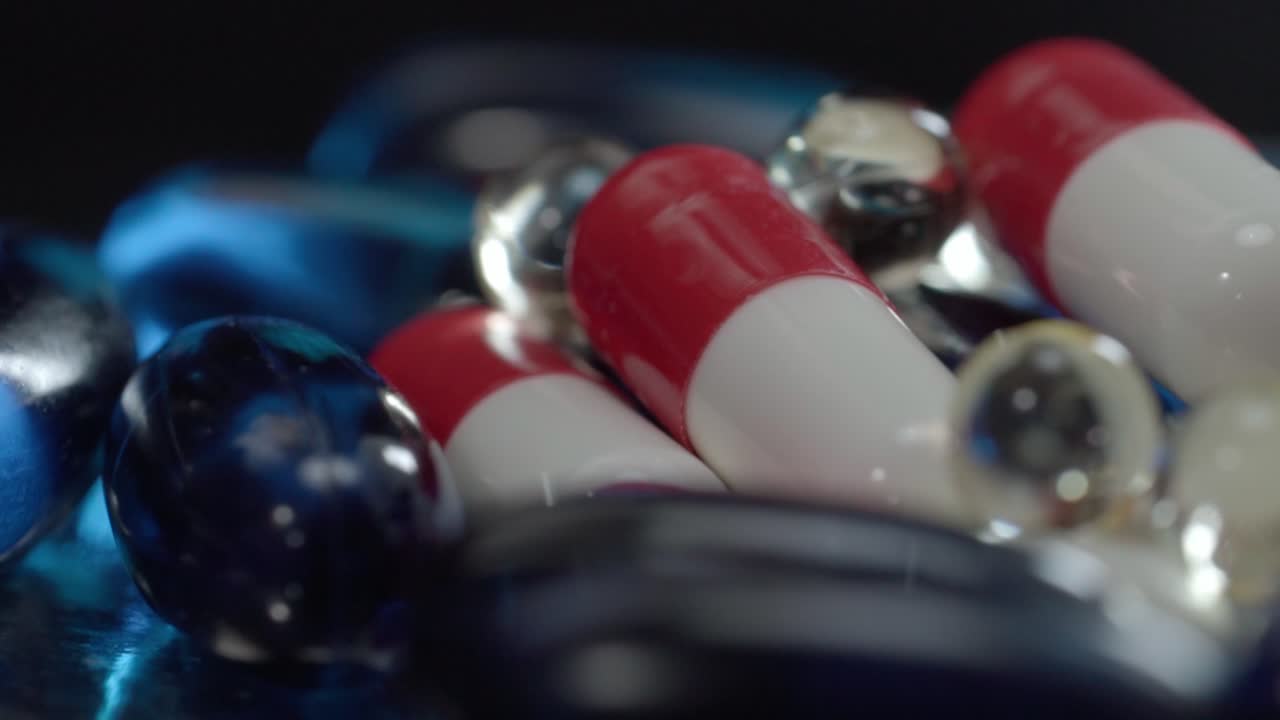 Close up of assorted red and white capsules with blue gel pills rotating on reflective surface