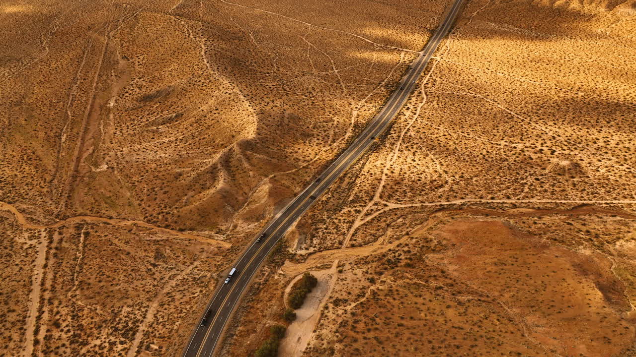 View of the highway with moving cars along the dry desert. Aerial perspective on the bare deserted landscape of Nevada.