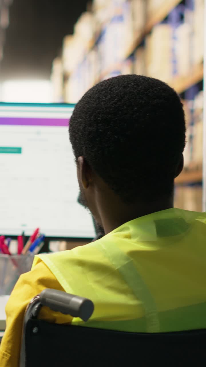 Video verticale. Uomo di colore in sedia a rotelle che utilizza software di tracciamento su una scrivania con PC.