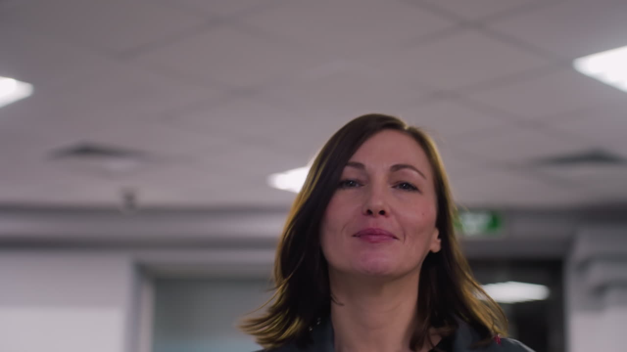 Smiling woman standing in office, professional environment, close-up of face, confident expression, positive mood, modern office lighting, workplace atmosphere, businesswoman in focus