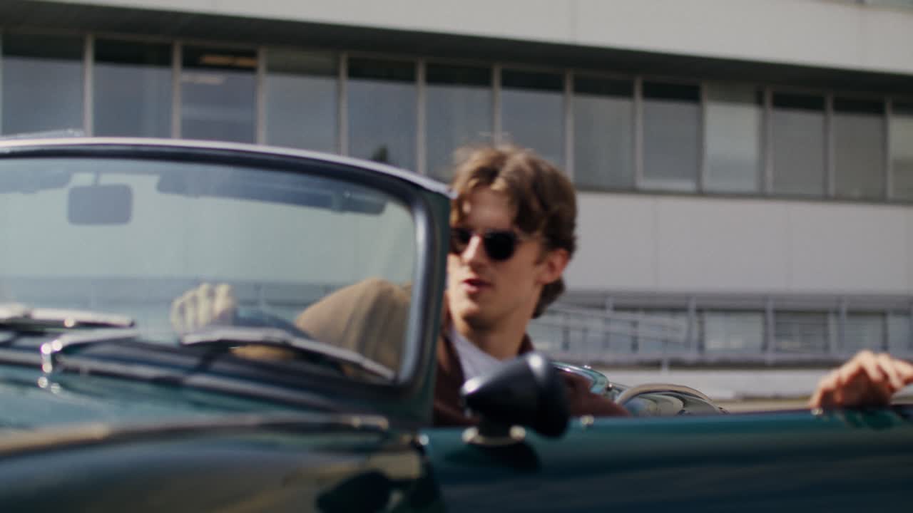 Couple in vintage convertible car in front of modern building