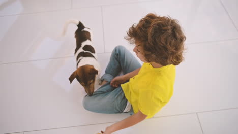 Draufsicht-Auf-Einen-Blonden-Jungen-Mit-Lockigem-Haar,-Der-Auf-Dem-Boden-Sitzt-Und-Mit-Seinem-Hund-Und-Einem-Ball-Spielt