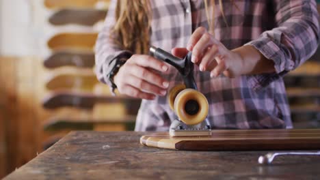 Video-Des-Mittelteils-Einer-Kaukasischen-Skateboarderin,-Die-Ihr-Skateboard-Im-Skateshop-Repariert