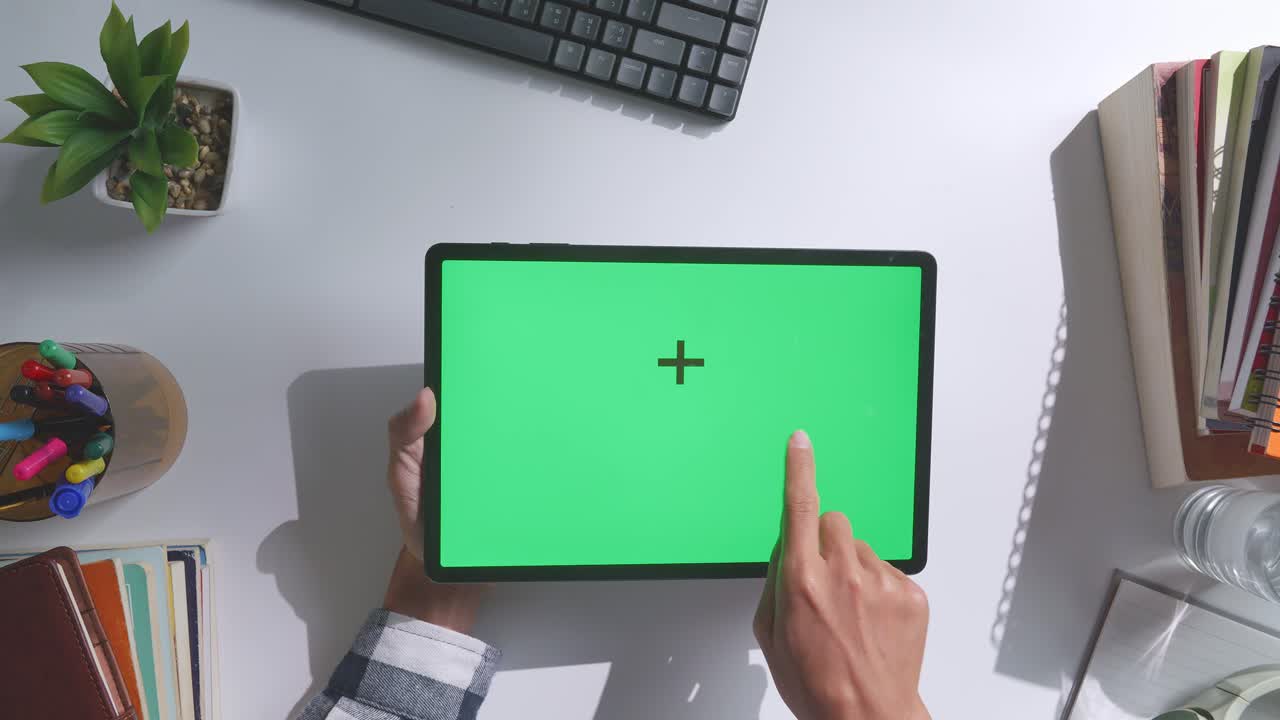 vista de arriba hacia abajo de una computadora portátil con pantalla verde simulada pantalla chromakey en un escritorio de oficina de madera al lado de la libreta con bolígrafos, gafas y un vaso de agua.