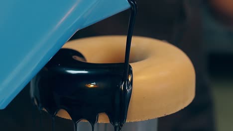 confectioner pours doughnut with dark liquid chocolate