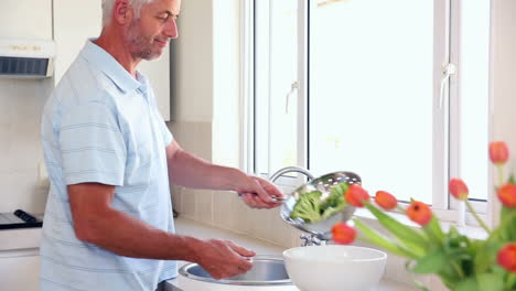 hombre feliz lavando brócoli en el fregadero